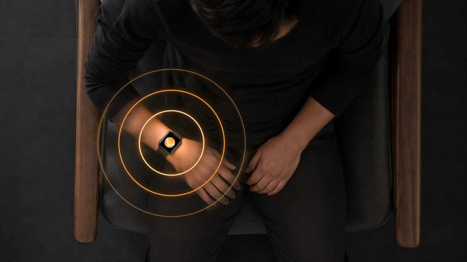 Overhead view of a seated person resting their hands in their lap, with concentric rings radiating from the AtLeast timer on their Apple Watch.